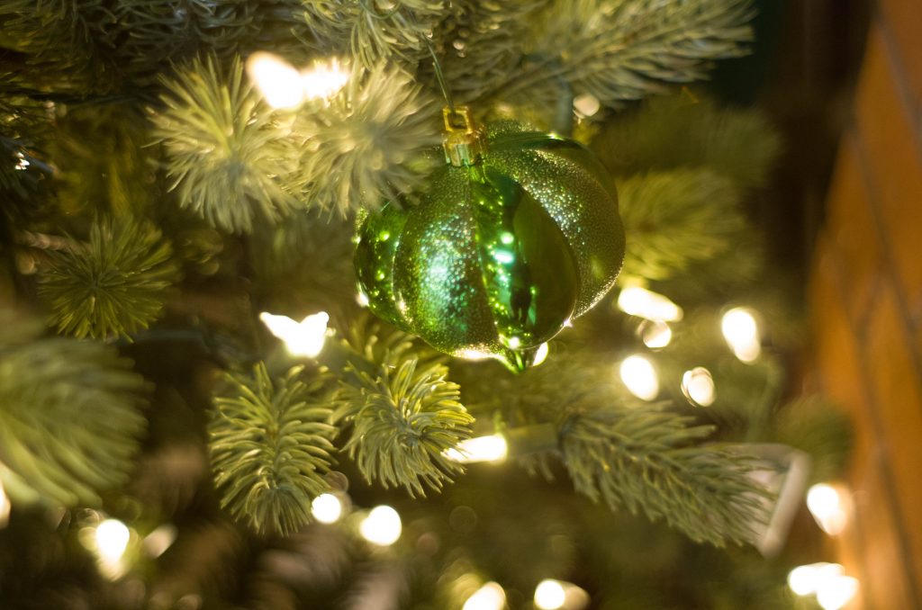 A green tree ornament with glitter and matte glass alternating on a lit pine tree.