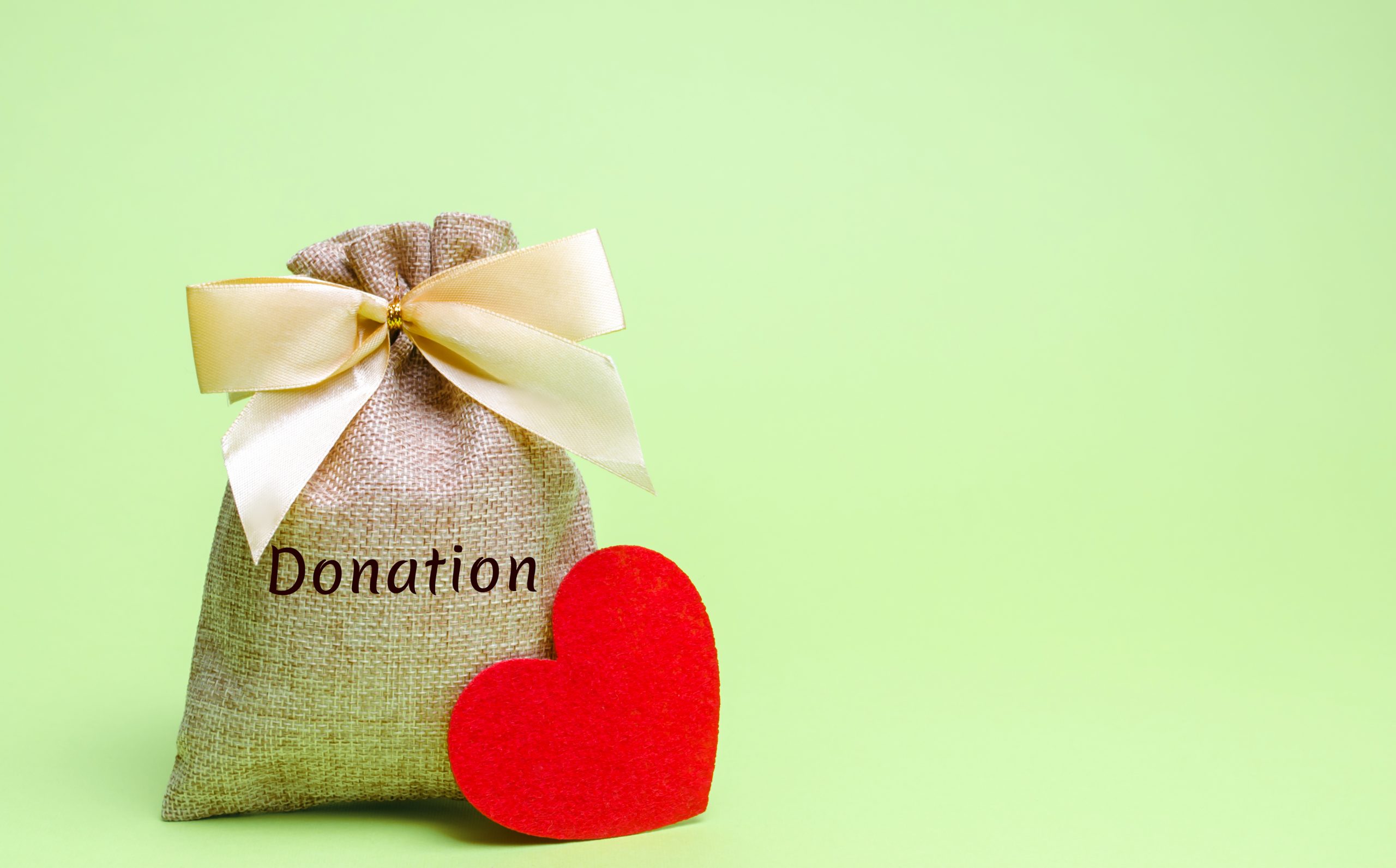 A money bag with the word Donation and a red heart on a pale green background to represent charitable giving. Image licensed through Adobe Stock.