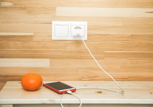 A charging smartphone and orange are lying on a bedside table. Image licensed by Adobe Stock.