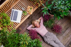 A top view of senior woman with laptop lying outdoors on terrace, resting. Image licensed through Adobe Stock.A top view of senior woman with laptop lying outdoors on terrace, resting.