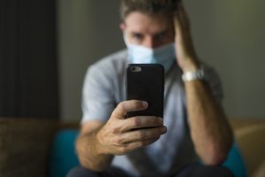 Man with face mask in home quarantine lockdown checking internet information. Image licensed through Adobe Stock.