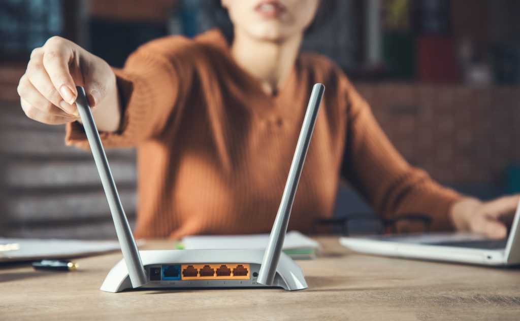 A person adjusting their router antennae while using a laptop. Image licensed through Adobe Stock.