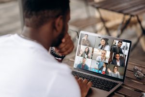 African American freelancer communicating by a video conference with his colleagues using a laptop while sitting in cafe in a summer terrace, Image licensed through Adobe Stock.