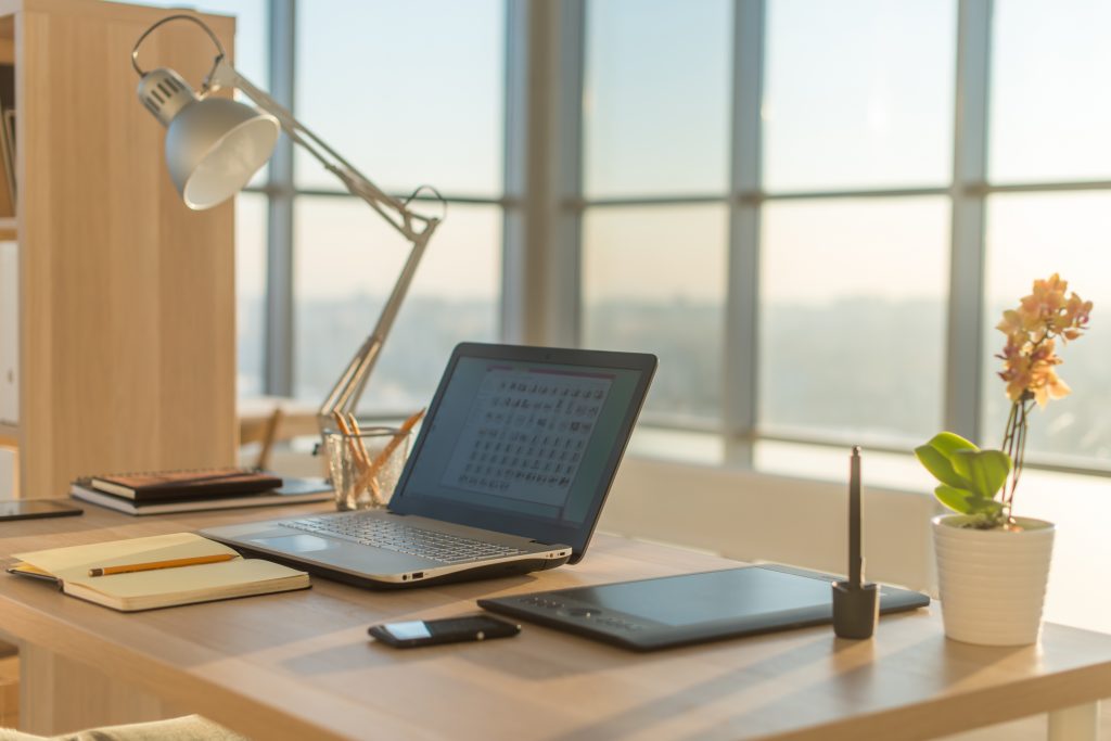 Side view picture of studio workplace with blank notebook, laptop. Licensed through Adobe Stock.