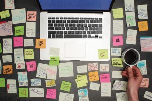 Top view on messy office desk with laptop, coffee and post it notes all around.. Licensed through Adobe Stock.