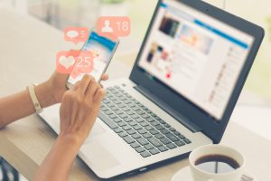 Young person using smart phone while at computer. Image licensed through Adobe stock.