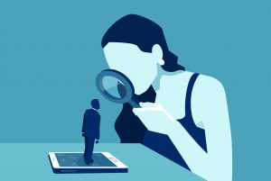 Vector of a woman with magnifying glass looking at a man standing on a modern gadget device, smartphone or tablet. Image licensed through Adobe Stock.