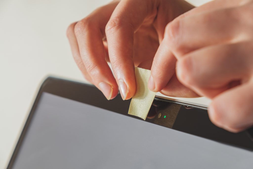 A person placing tape over their webcam. Image licensed through Adobe Stock.