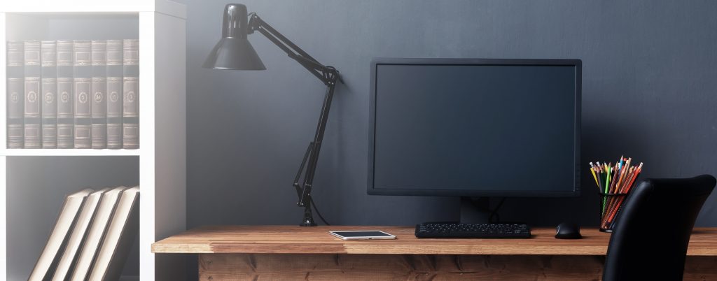 A computer desk with a monitor, keyboard, mouse, and lamp all turned off. Image licensed through Adobe Stock.