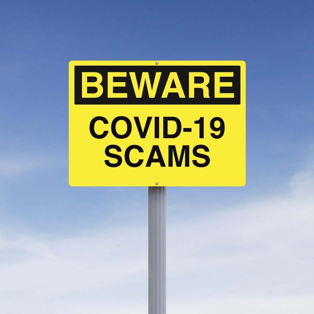 A yellow traffic sign with black text on a blue sky background that says "Beware COVID-19 Scams." Image licensed through Adobe Stock.